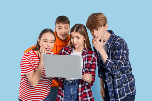 Group of teenagers using laptop on light blue background