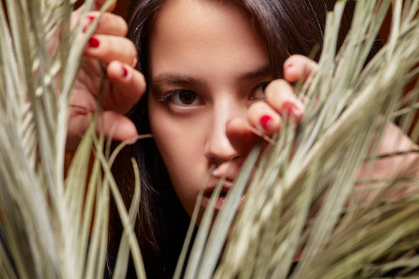A woman peeping out from behind a palm leaf.