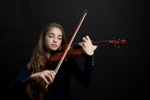 Young beautiful girl playing violin on black background, studio shot