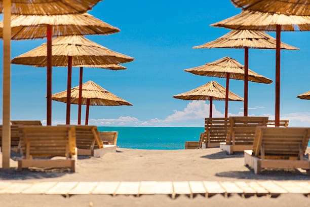 Tropical resort sandy beach soft selective focus. Beach with sun umbrellas and deck chair or sunbeds on bright clear day. Summer vacation on sea beach. Mountains near sandy beach