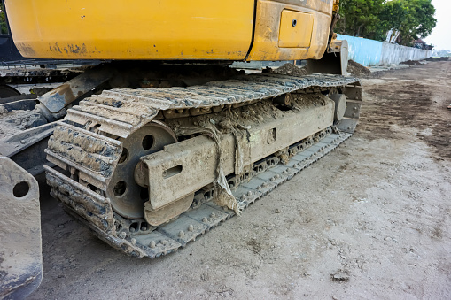 Continuous tracks of a dirty excavator in a construction site. Close up