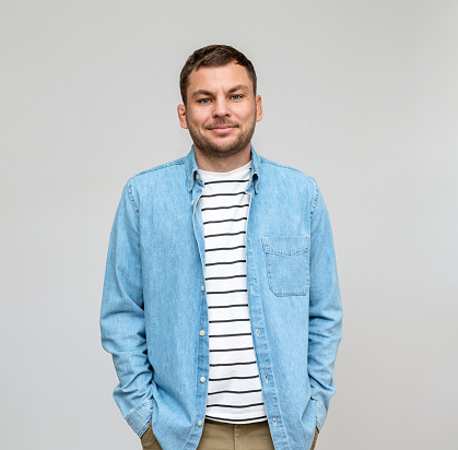 Portrait of man casual wearing in jeans shirt and striped t-shirt smiles in front of plain background in studio.