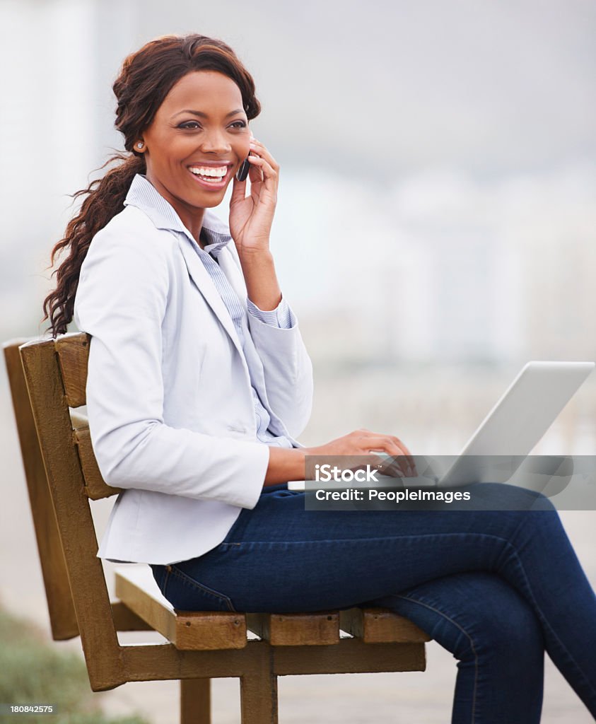 Outdoor office! A modern professional working on her laptop on a park bench at the promenade Cheerful Stock Photo