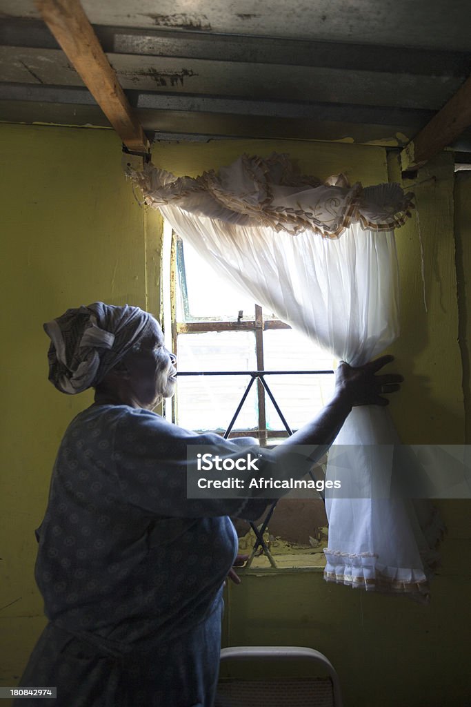 Looking Out the Window, Gugulethu, Cape Town, South Africa. "Elderly lady looking out the window of her house, Gugulethu, Cape Town, Western Cape, South Africa." Looking Through Window Stock Photo