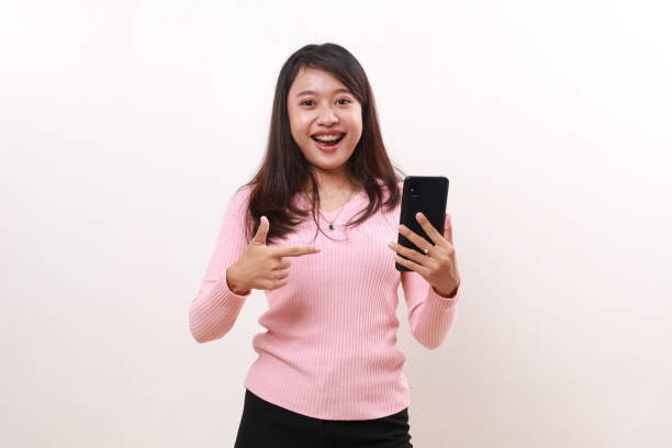 istock Wow excited young asian girl standing while pointing a blank cell phone screen. Isolated on white background 1808447643