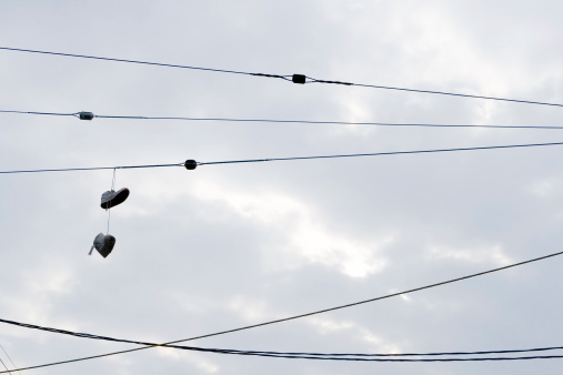 shot of shoes hanging off overhead powerlines against a cloudly sky background