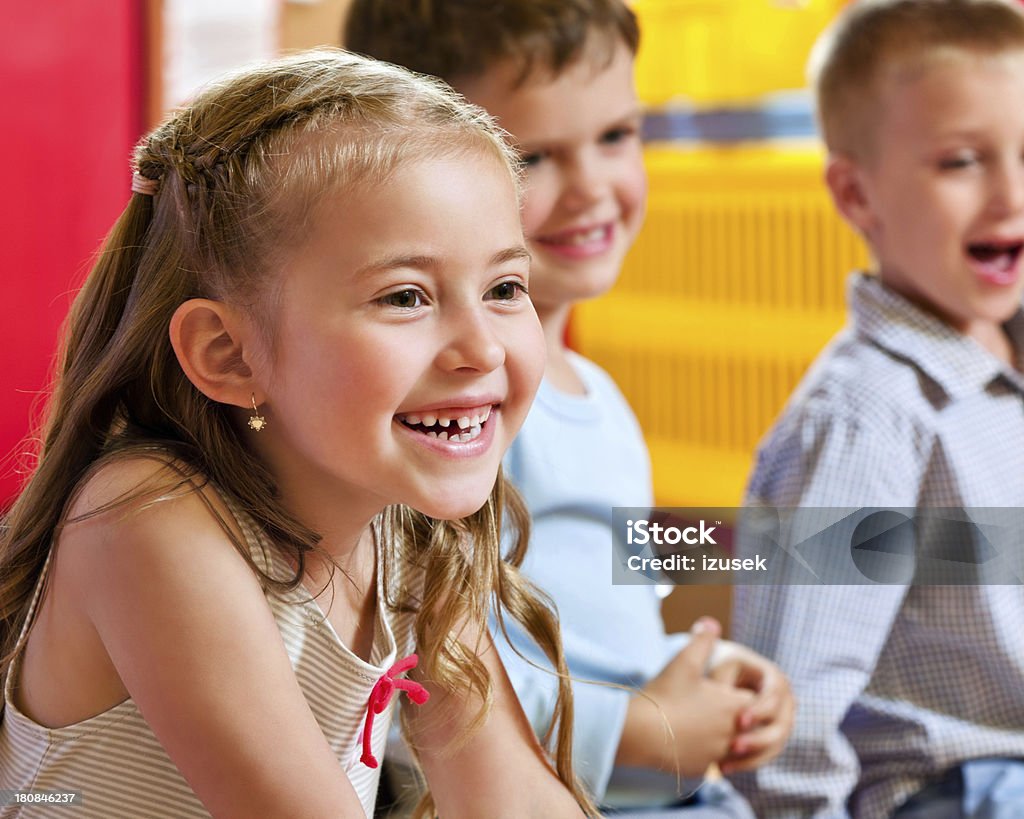 Cute Nursery School Children Focus on the cute little girl sitting in a playroom with her friends in the background and laughing. 4-5 Years Stock Photo