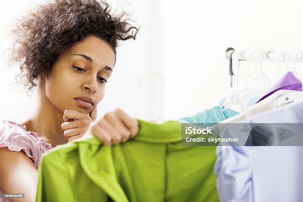 Young woman thinking what to buy. African-American young woman is shopping in a boutique. Clothing Store Stock Photo