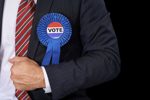 Cropped view of a man in a suit wearing a voting ribbon ona black background