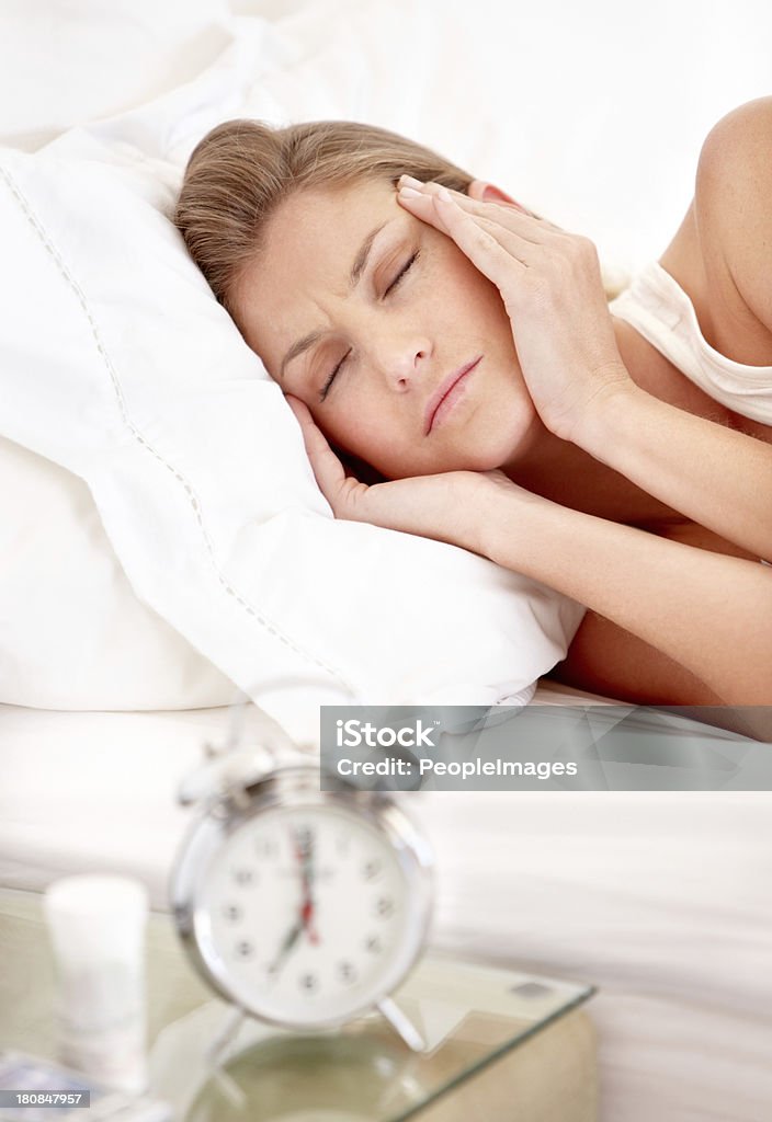 This headache is bad A young woman massaging her temples while lying in bed with a headache Insomnia Stock Photo