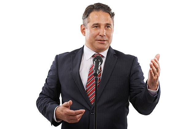 A man in a suit with his hands raised while saying a speech into a microphone