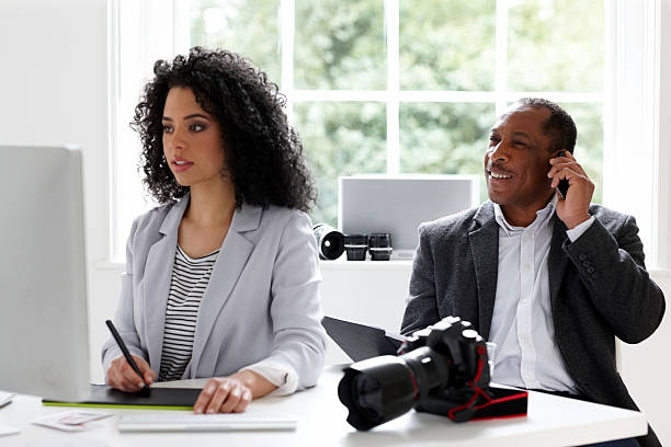 Female photo retoucher working with her mentor talking on mobile phone in background