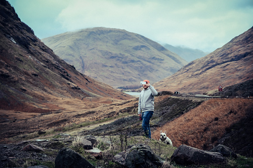 Man with his dog at The Three Sisters of Glencoe, taking photo with his smart phone