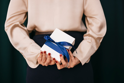 Close up shot of an unrecognizable woman holding a gift box behind her back.