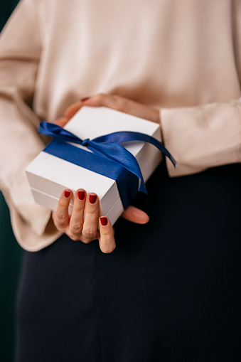 Close up shot of an unrecognizable woman holding a gift box behind her back.