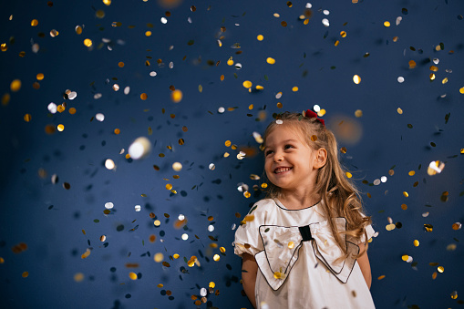Close up shot of a young girl standing while the glitter is in the air falling around her. She is looking away and smiling.