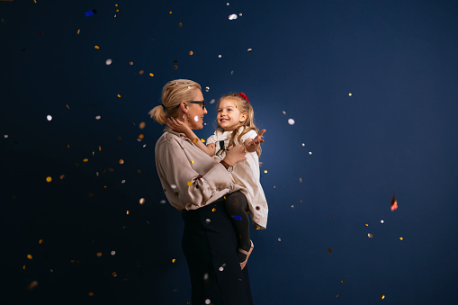 Happy little girl and her mom having fun together while confetti falling down during a Christmas celebration.
