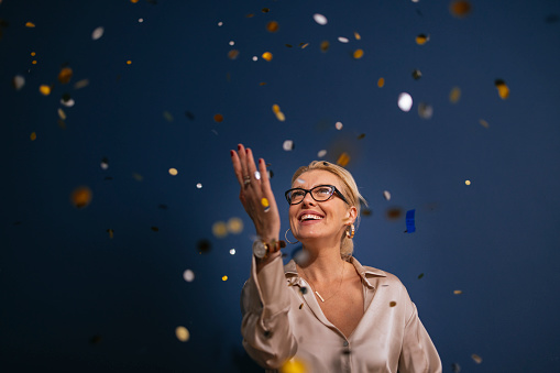 Happy elegant woman having fun while confetti falling down during a New Year celebration.