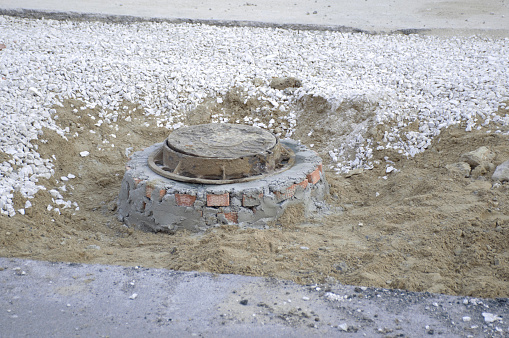 a closed hatch, destroyed asphalt, sand and rubble remained after the road was repaired. maintenance, repair and replacement of city communications, underground pipes and cables