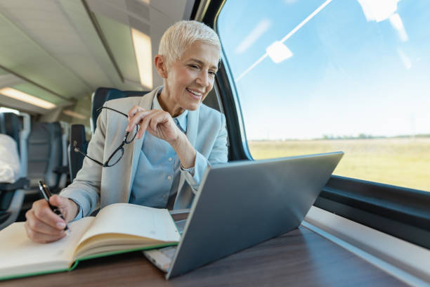Senior businesswoman using laptop and writing notes in the train