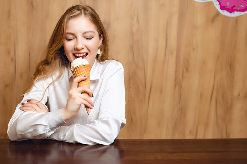 Funny portrait of a young woman who eating ice cream indoors. A person in the cafe enjoying food.
