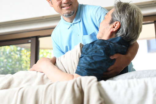 An Asian male caregiver woke up a bedridden elderly man.