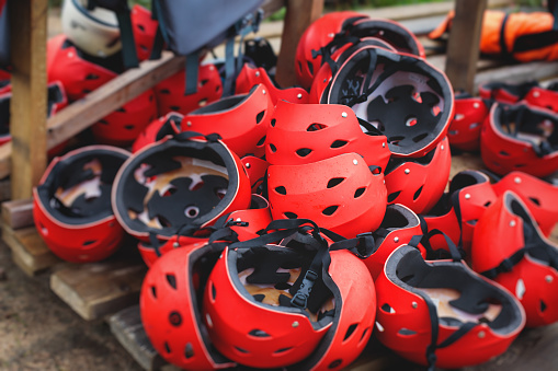 Equipment for water sports: bunch of wetsuits, paddles, red helmets and life jackets, preparing for rafting, kayaking, canoeying and stand up paddle, preparing to extreme water sports and tourism