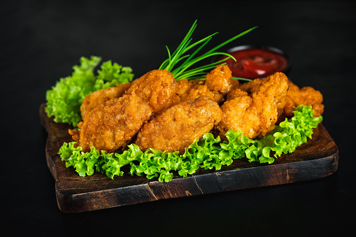 Fast food. Breaded chicken nuggets.Chicken wings fried until half cooked, semi-finished product.Semi-finished chicken wings on a dark background with fresh herbs. Half-finished.Quick cooking at home. Fast food. Breaded chicken wings.
