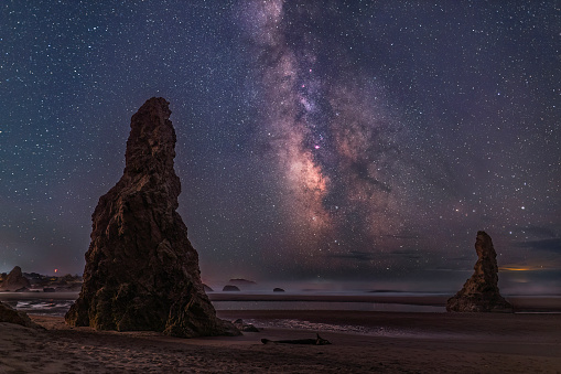 The Milky Way stretches out of the Pacific Ocean between two sea stacks on Bandon Beach, Oregon.