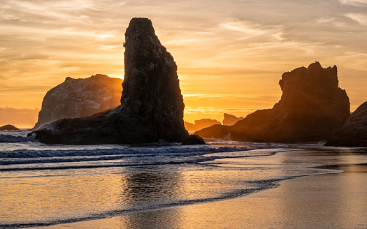 Golden light surrounds sea stacks, reflected in the Pacific Ocean on Bandon Beach in Bandon, Oregon