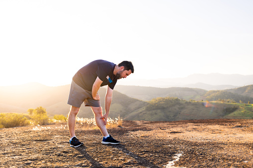 Brazilian mid-adult readies for a run, epitomizing fitness. Image conveys exercise preparation, inspiring a healthy life through sports. Set against a scenic backdrop with a beautiful sunset