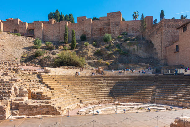 Tourists at the Roman Theatre and Alcazaba in Málaga; Spain; Tourists visiting the 1st century AD semicircular Roman Theatre blow the fortified walls of the Alacazaba in Málaga, Spain. Tha Alcazaba is a palace-fortification built in the 11th century BCE and added to until the 14th century. alcazaba of málaga stock pictures, royalty-free photos & images