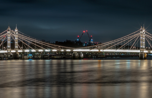 London, UK - Nov 20, 2023 - Nocturnal view of floodlit Albert Bridge from Chelsea Bridge with the reflection of the light in very calm water. Lit up at Night Illuminated Albert bridge in west London at night, Copy space, Selective Focus.