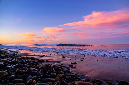 This is a beautiful sunrise photo taken early in the morning at moonlight beach California with the waves coming in on the shore with the colorful magenta orange sand reflection of the sun.