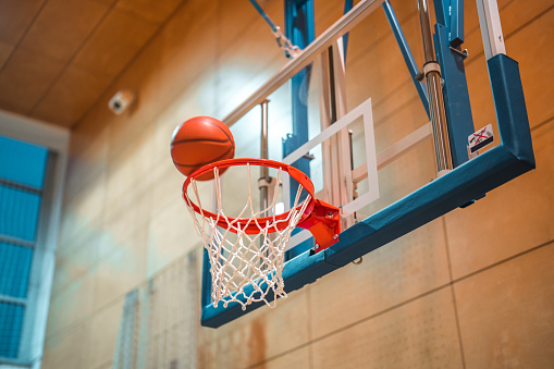 Basketball hoop and a basketball on it in a sports hall.