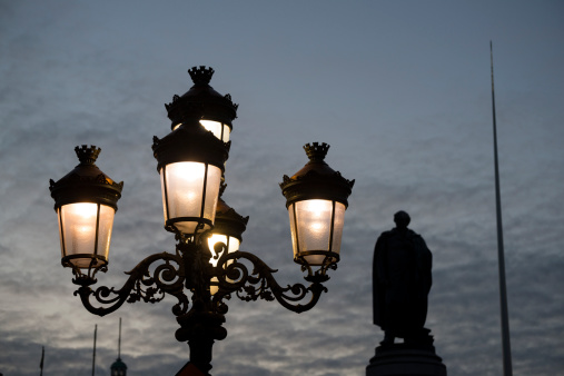 Lamps shine in the evening sky on O'Connell Street in central Dublin, Ireland. The O'Connell Monument and the Spire of Dublin (also called the Monument of Light) are in the background.