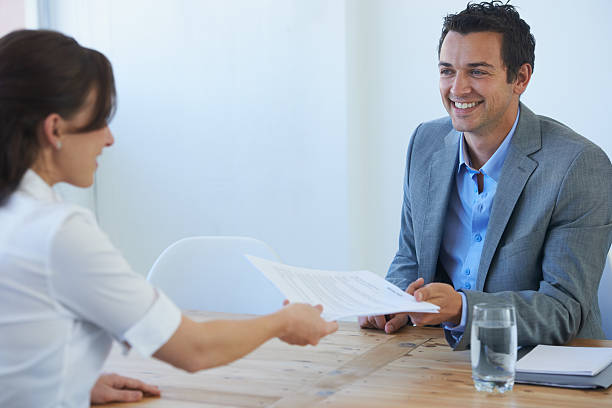 Let's see that resume... A smiling businessman receiving a resume from a young woman at a job interview passing giving stock pictures, royalty-free photos & images