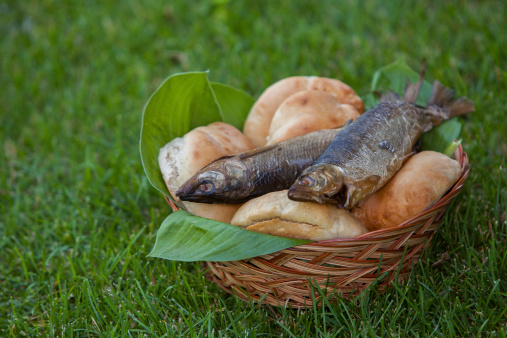 a basket with 5 loaves of bread and 2 fish lying on the grass, symbolic of the Bible story where JESUS CHRIST multiplied 5 loaves and 2 fish to feed the 5000 people who were following him and listening to his teachings.