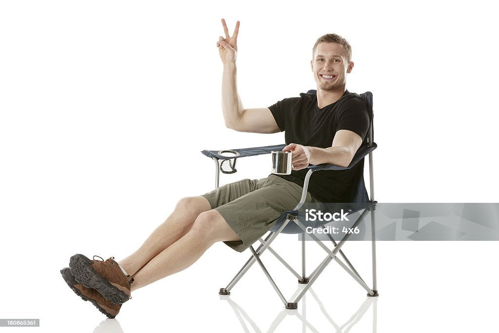Молодой человек, сидя на стуле Жестикулировать Знак Победы - Стоковые фото Кресло-шезлонг роялти-фри