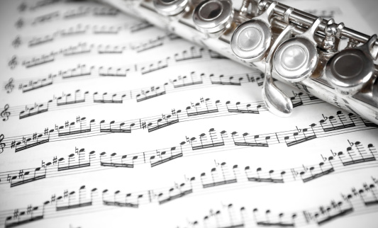 Close up of a silver flute on a sheet of music notes. Black and white strong contrast and vignette effect.