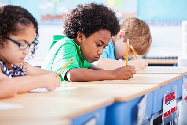 Elementary school children writing in class Multi-ethnic elementary school children writing in classroom.  Focus on African American boy (8-9 years). primary school exams stock pictures, royalty-free photos & images