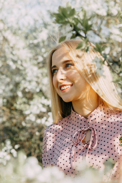 Blonde girl on a spring walk in the garden with cherry blossoms. Female portrait, close-up. A girl in a pink polka dot dress. stock photo