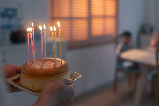 Close up behind of a father holding a birthday cake with the candles lit at an indoor party celebration