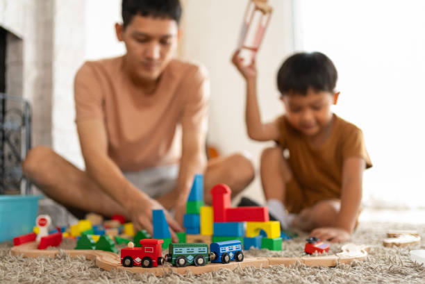 Asian kid is playing with toy train on the railway on the floor with father
