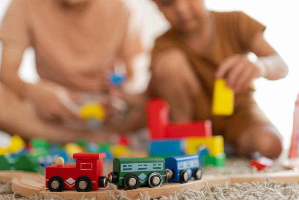 Asian kid is playing with toy train on the railway on the floor with father