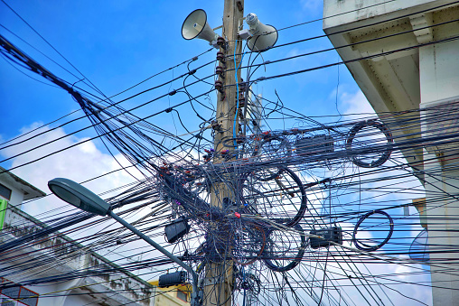 Messy wires on the pole chaos of cables Internet cables and wires on electrical poles in Thailand with a building in the background sky and clouds