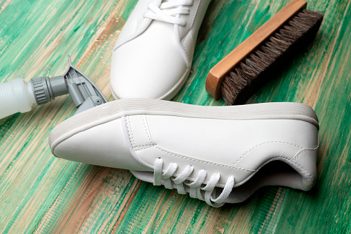 Brush and bottle sprayer with white sneakers on a wooden background. Shoe care concept