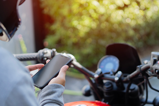 Close up photo of motorcycle or maxi scooter driver in helmet use smartphone application to find geo location. Selective focus on hands.