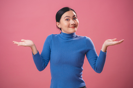 Asian woman angry annoyed and shrugging shoulders standing isolated over pink background.