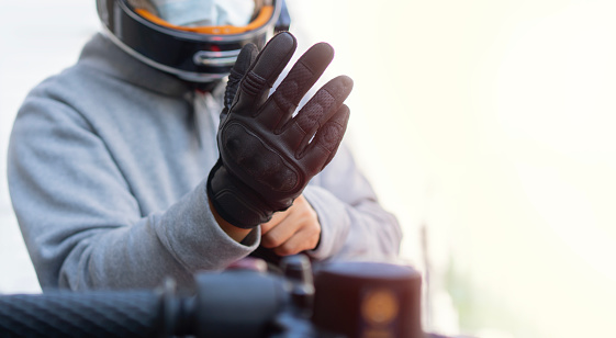 Cropped image of biker putting on leather gloves to drive his motorbike. Selctive focus, copy space.